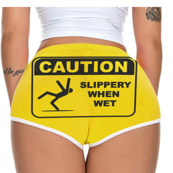 Stylish yellow booty shorts with bold "CAUTION SLIPPERY WHEN WET" warning graphic, made by Vegas Style fashion brand for eye-catching, statement casual wear.